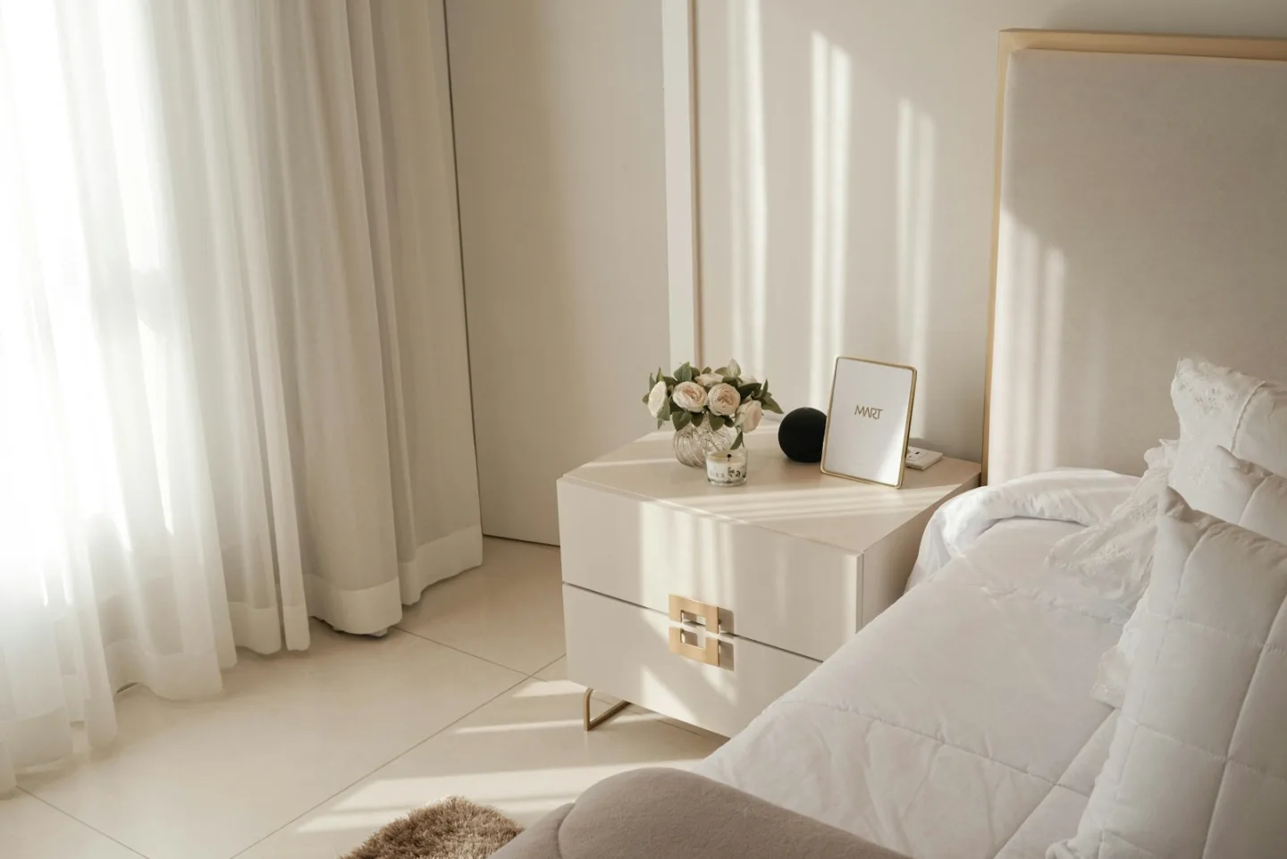 Bright, airy bedroom with layered white bedding, soft daylight, and a polished finish